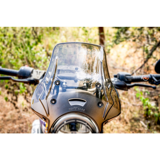 Close-up of motorcycle windscreen with handlebars, clear shield and forest background