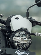 Close-up motorcycle headlight with protective grill, custom windshield, handlebar, and indicator