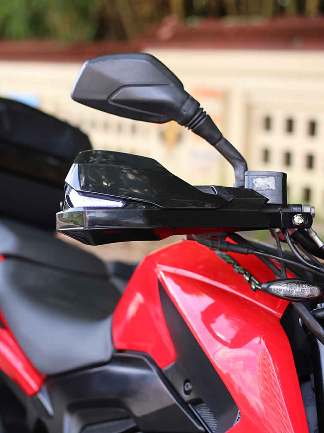 Close-up of red motorcycle handlebar with black mirror and handguard