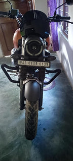 Front view of a black and orange motorcycle with round headlight and visible license plate indoors