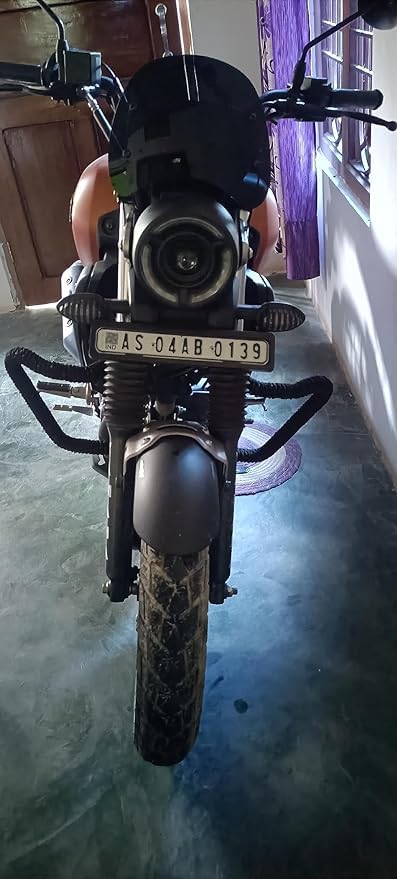 Front view of a black and orange motorcycle with round headlight and visible license plate indoors