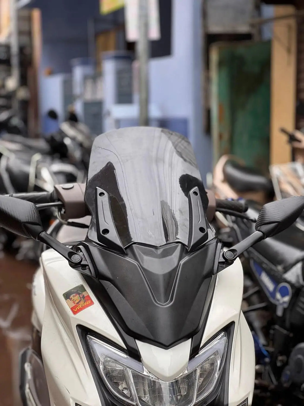 Close-up of a white scooter with a tall tinted windshield, parked on a city street.
