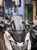 Close-up of a white scooter with a tall tinted windshield, parked on a city street.