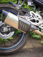 Close-up of a motorcycle rear wheel and exhaust pipe on outdoor pavement
