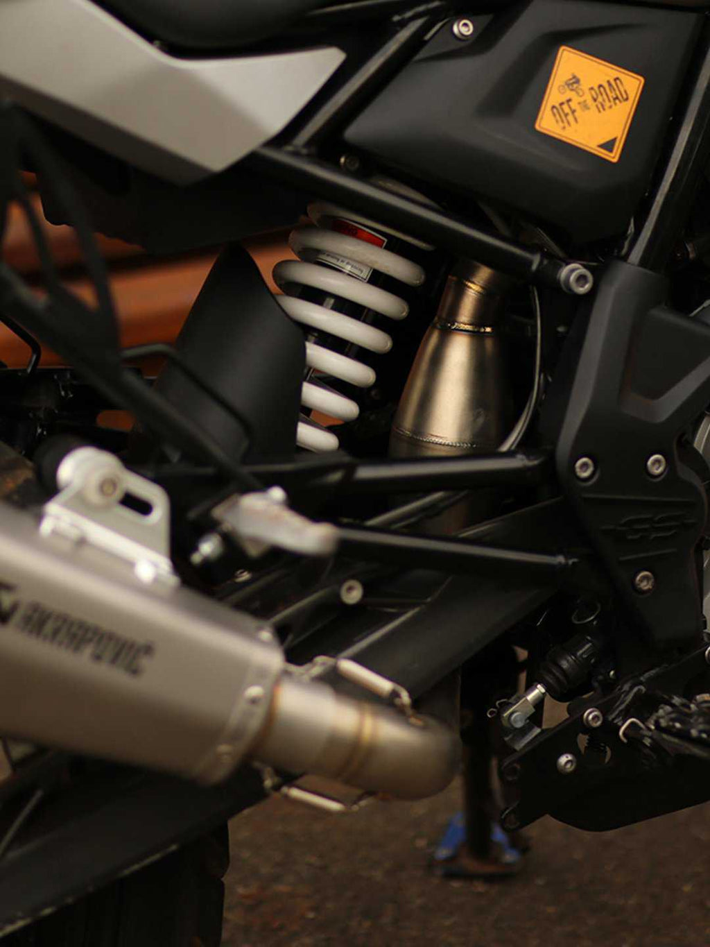 Close-up of BMW motorcycle rear suspension, exhaust pipe, Akrapovic muffler, and off-road decal