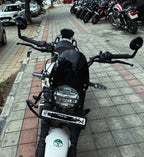 Front view of a parked black and white motorcycle on a city sidewalk, with other bikes lined up in the background.