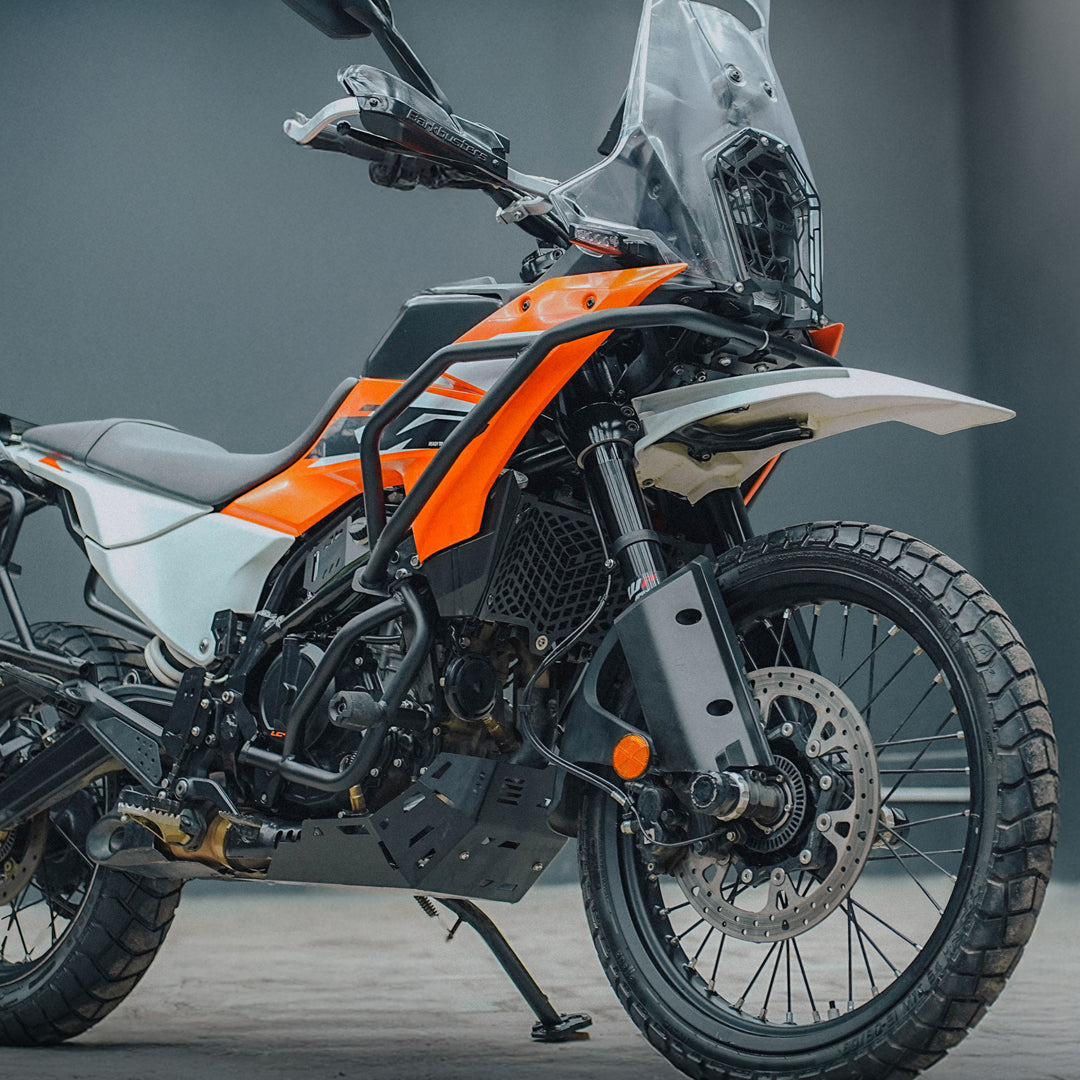 Orange and white adventure motorcycle with crash guards and off-road tires in a studio
