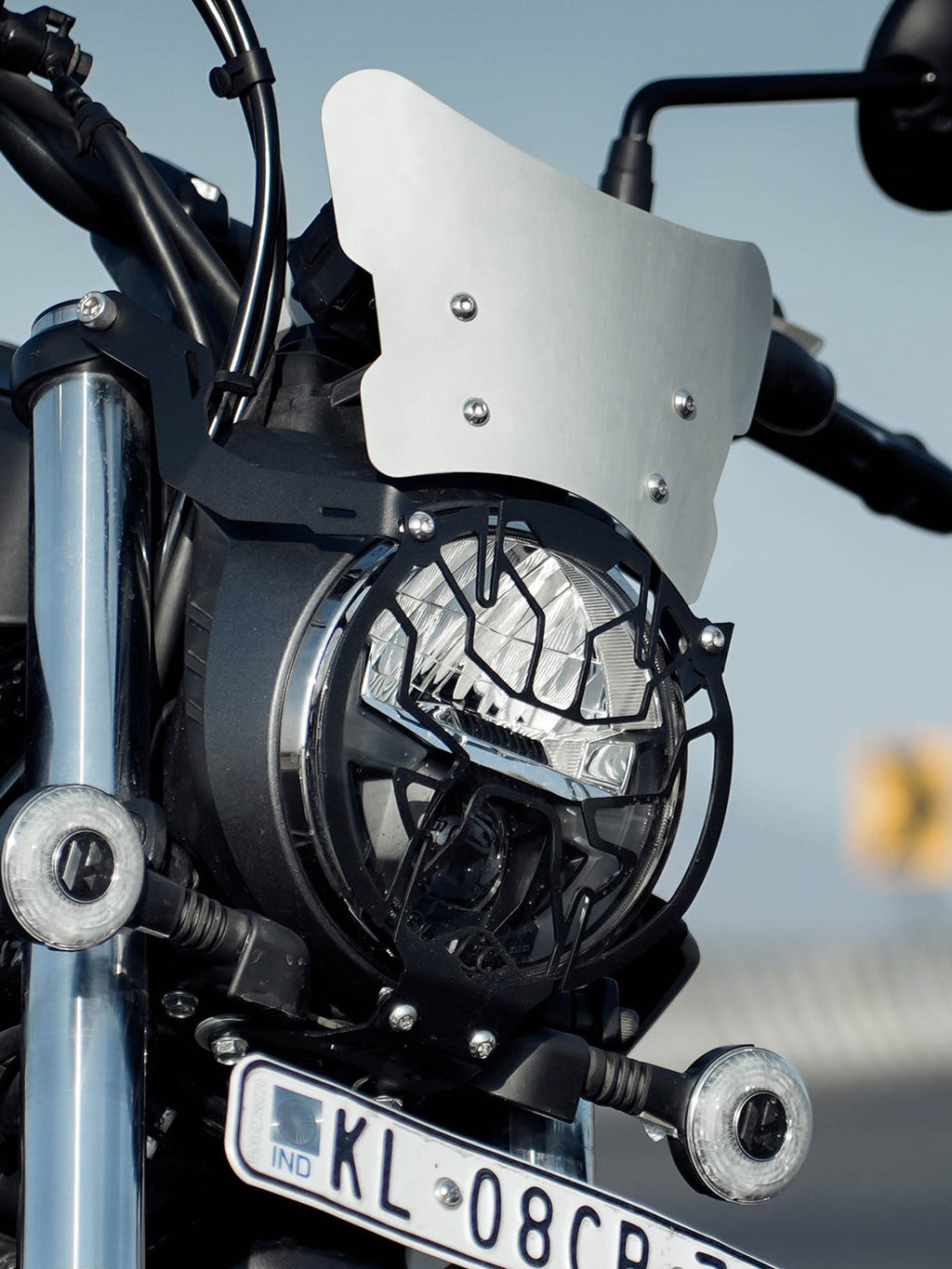 Motorcycle front view with headlight grill, silver windscreen, and license plate