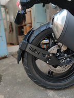 Close-up of BMW motorcycle rear wheel, disc brake, tire, and exhaust pipe.