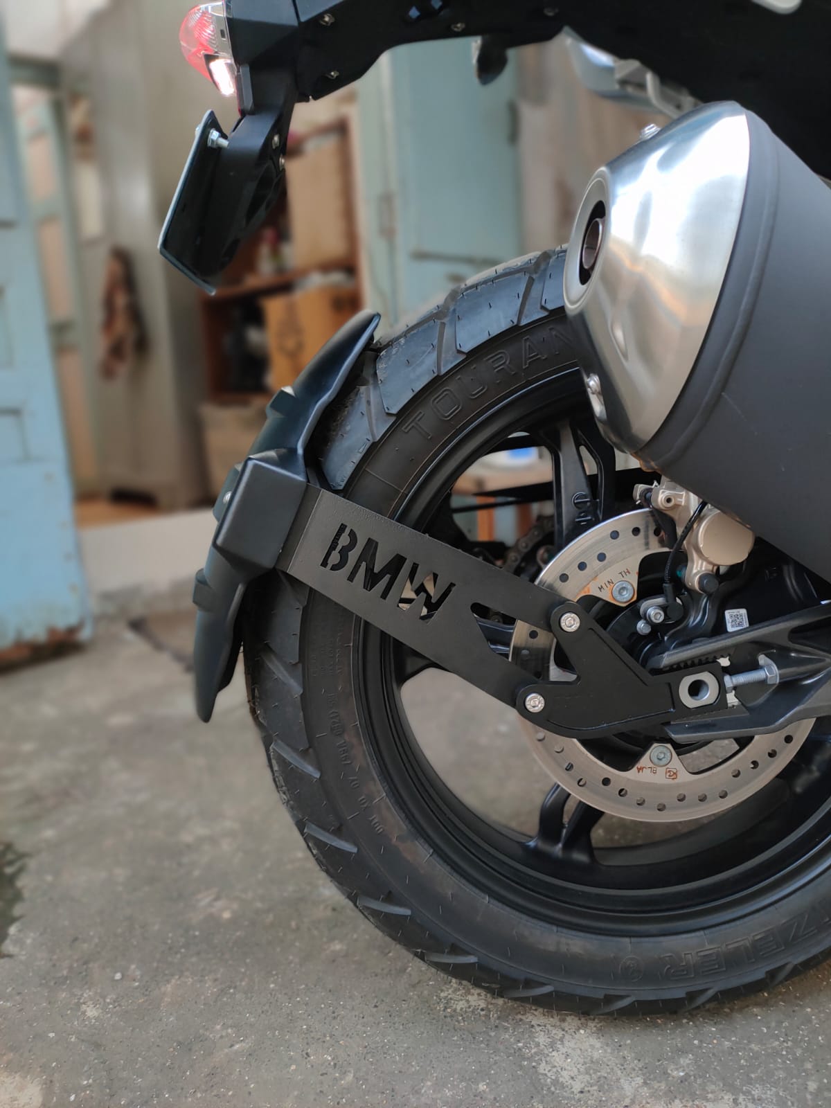 Close-up of BMW motorcycle rear wheel, disc brake, tire, and exhaust pipe.