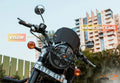 Motorcycle with black headlight grill and visor, labeled, parked outdoors in city setting