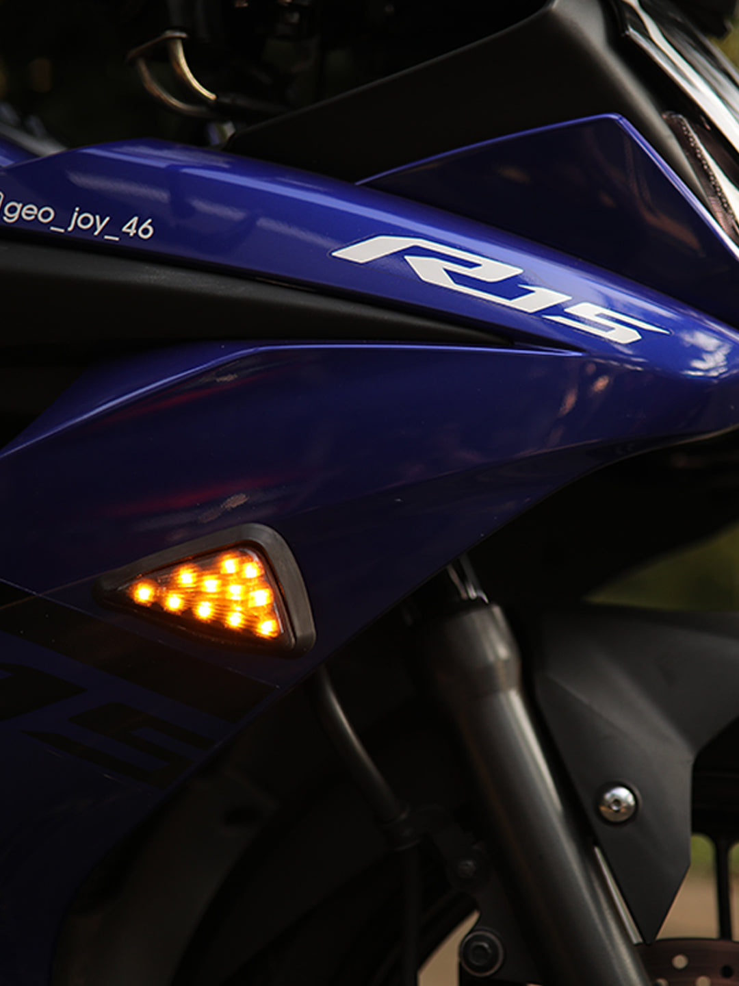 Close-up of blue motorcycle fairing with R15 decal and amber LED flush mount turn signal.
