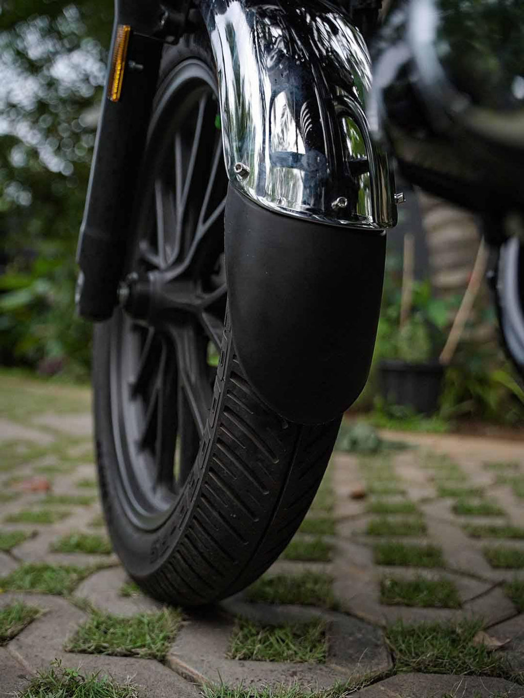 Close-up of motorcycle front wheel with a chrome mudguard extender on a paved path