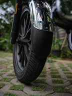 Close-up of motorcycle front wheel with a chrome mudguard extender on a paved path