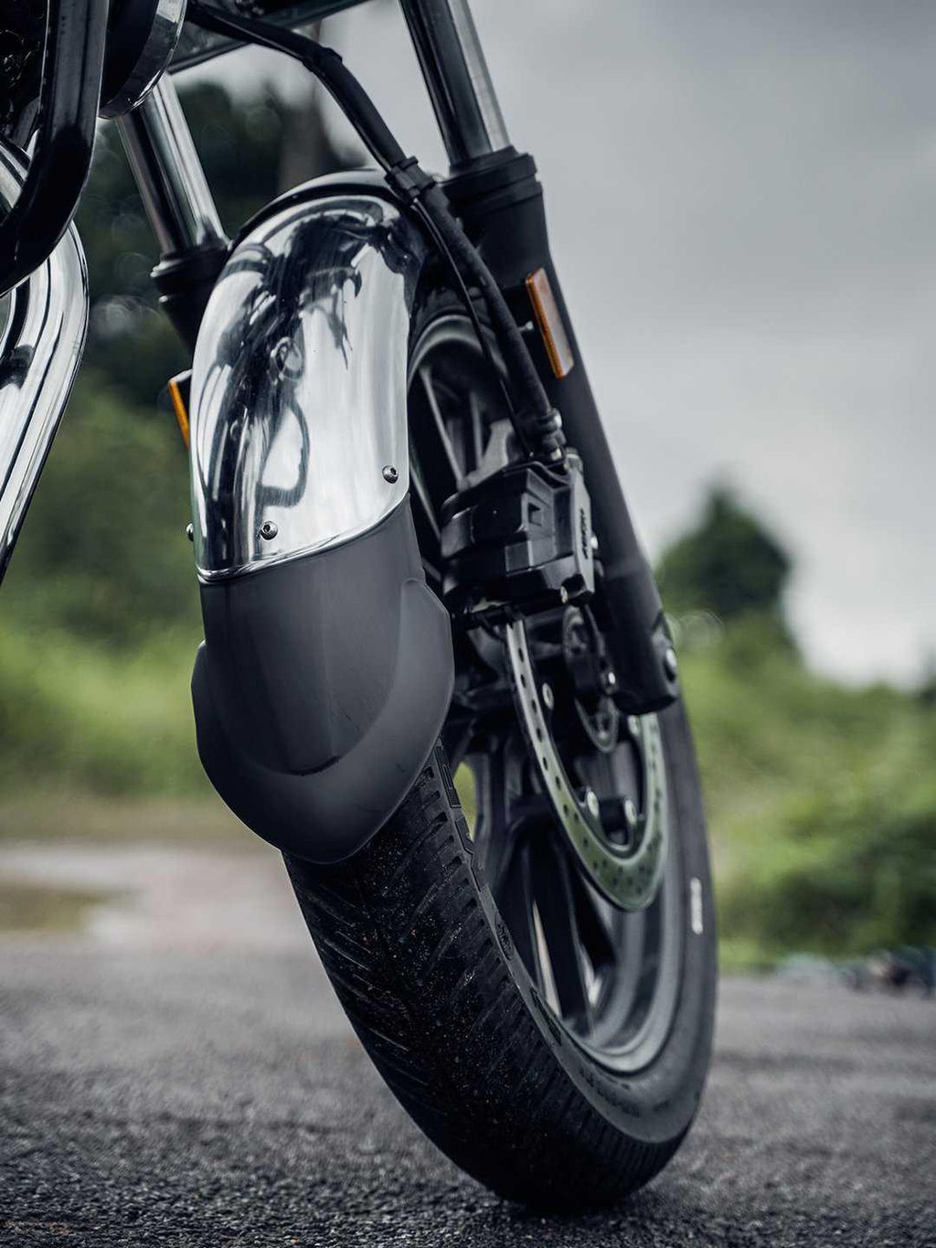 Close-up of motorcycle front wheel with chrome mudguard extender on wet road outdoors
