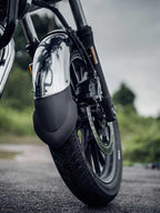 Close-up of motorcycle front wheel with chrome mudguard extender on wet road outdoors