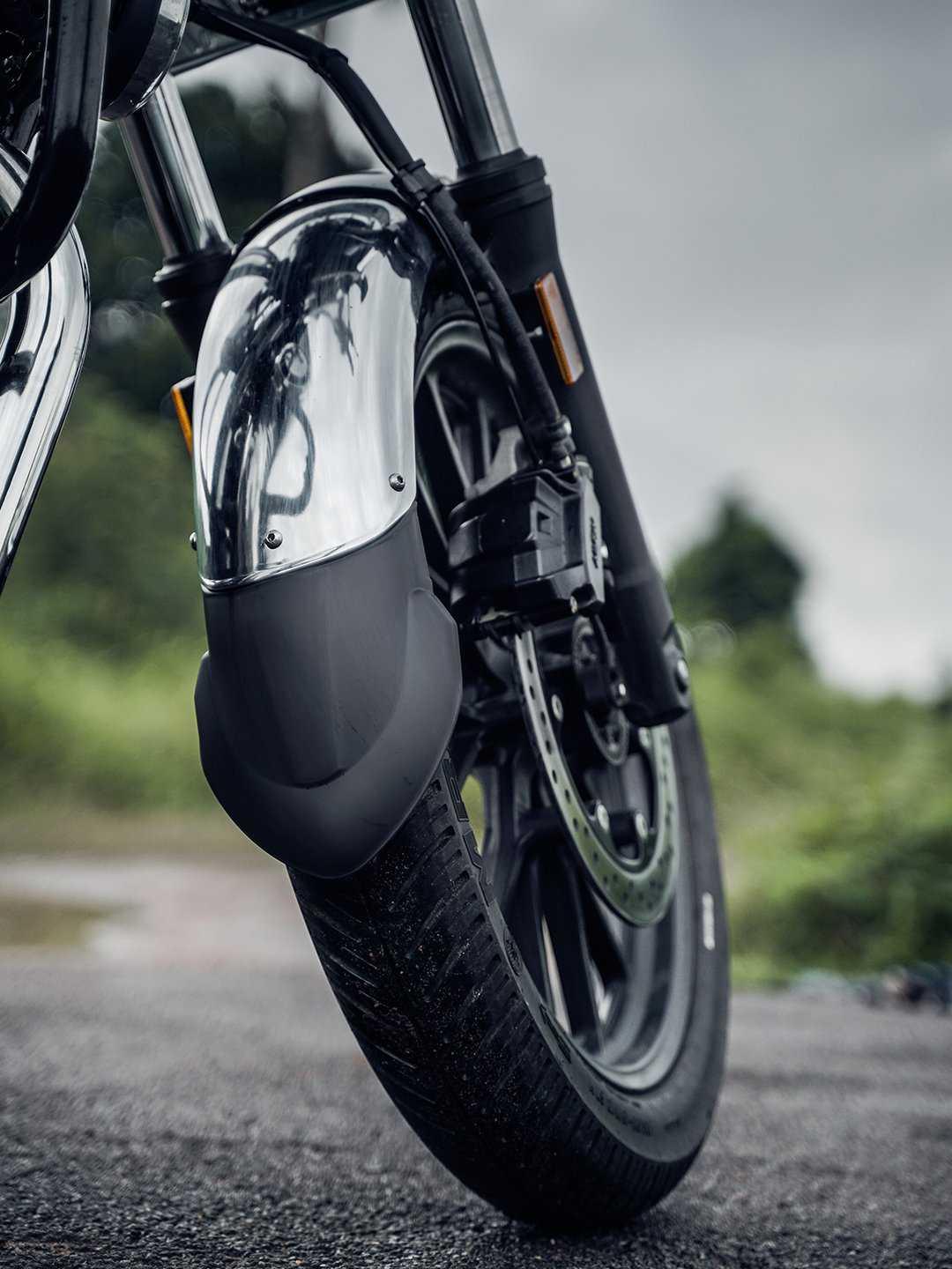 Close-up of motorcycle front wheel with chrome mudguard extender on wet road outdoors
