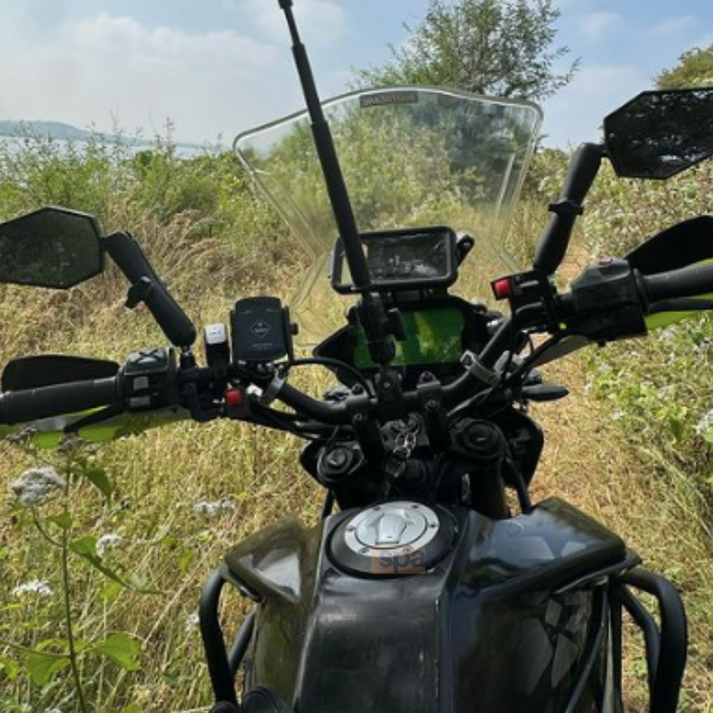 Motorcycle handlebars with windshield, mirrors, and GPS device in an outdoor grassy area