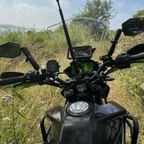 Motorcycle handlebars with windshield, mirrors, and GPS device in an outdoor grassy area