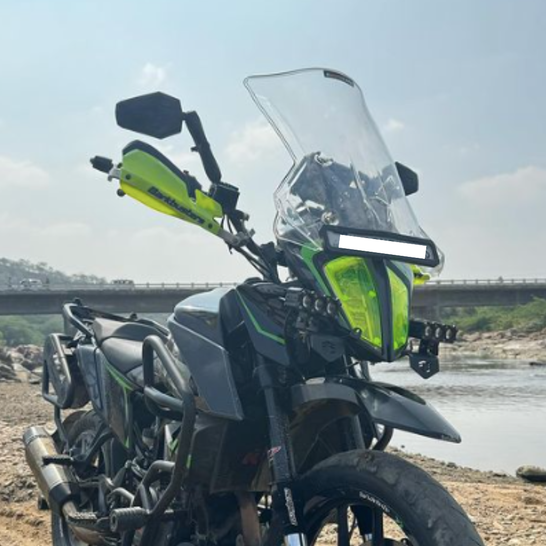 Adventure motorcycle with tall windshield, bright yellow handguards, and river backdrop